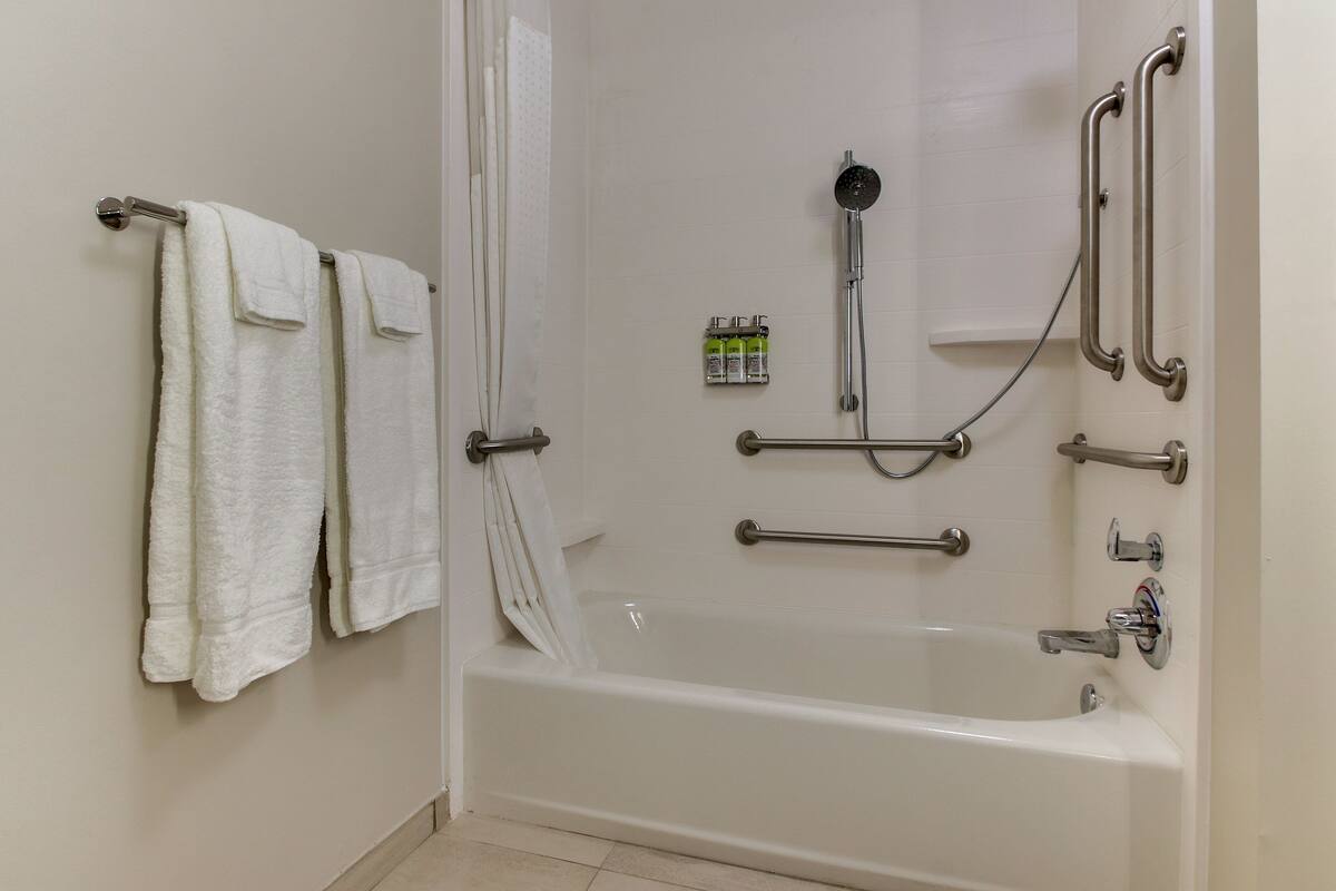 A bathroom with a bathtub, handrails, and a towel rack.