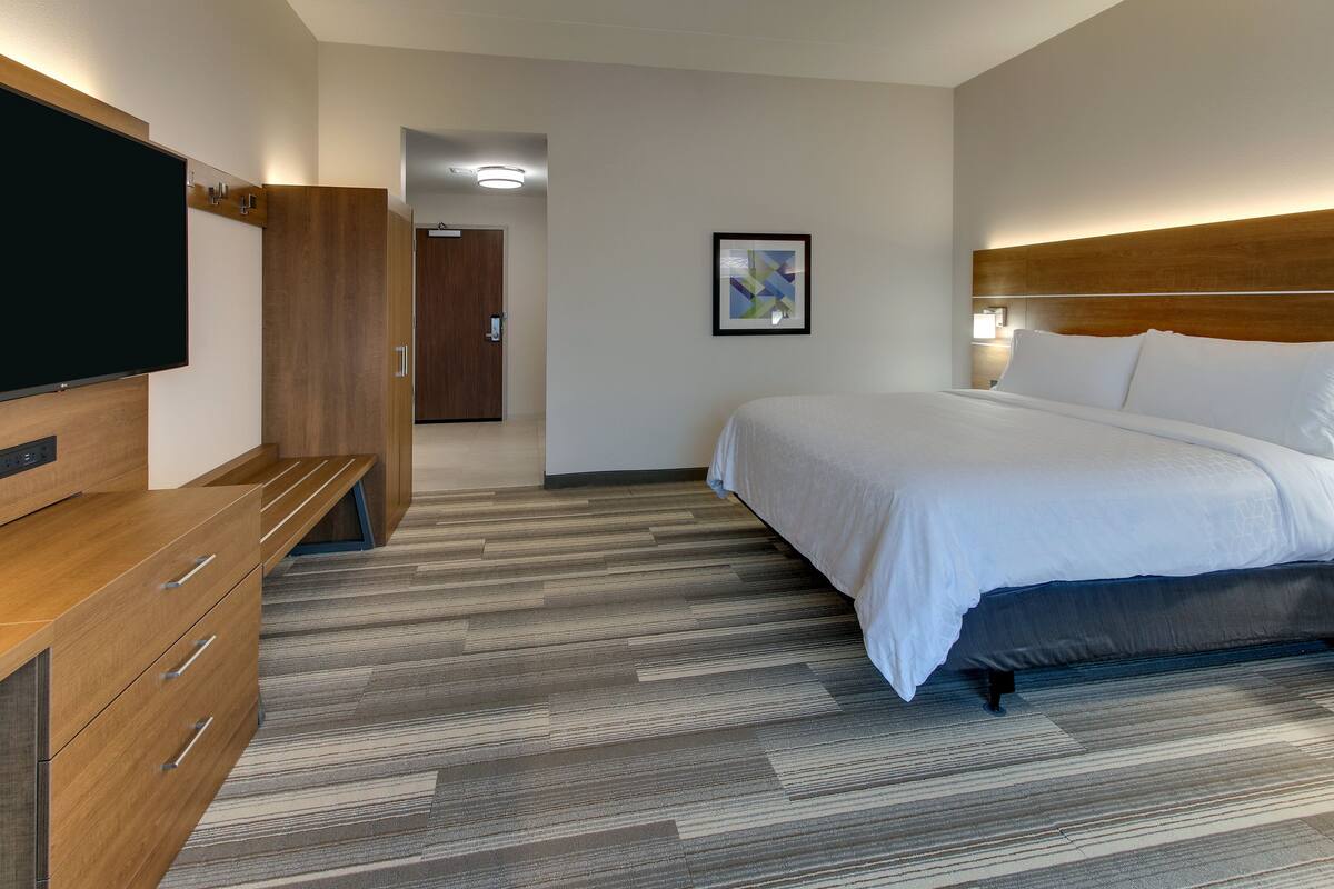 A hotel room with a bed, a TV, a wooden dresser, and a framed picture on the wall.