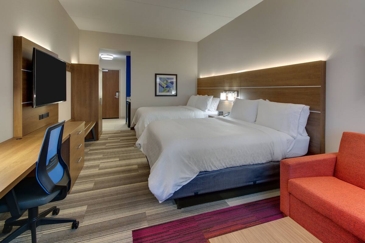 A hotel room with a bed, a desk with a chair, a television, and a red sofa.