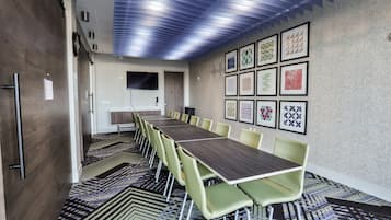 A conference room with a long table, green chairs, patterned carpet, and framed wall art.