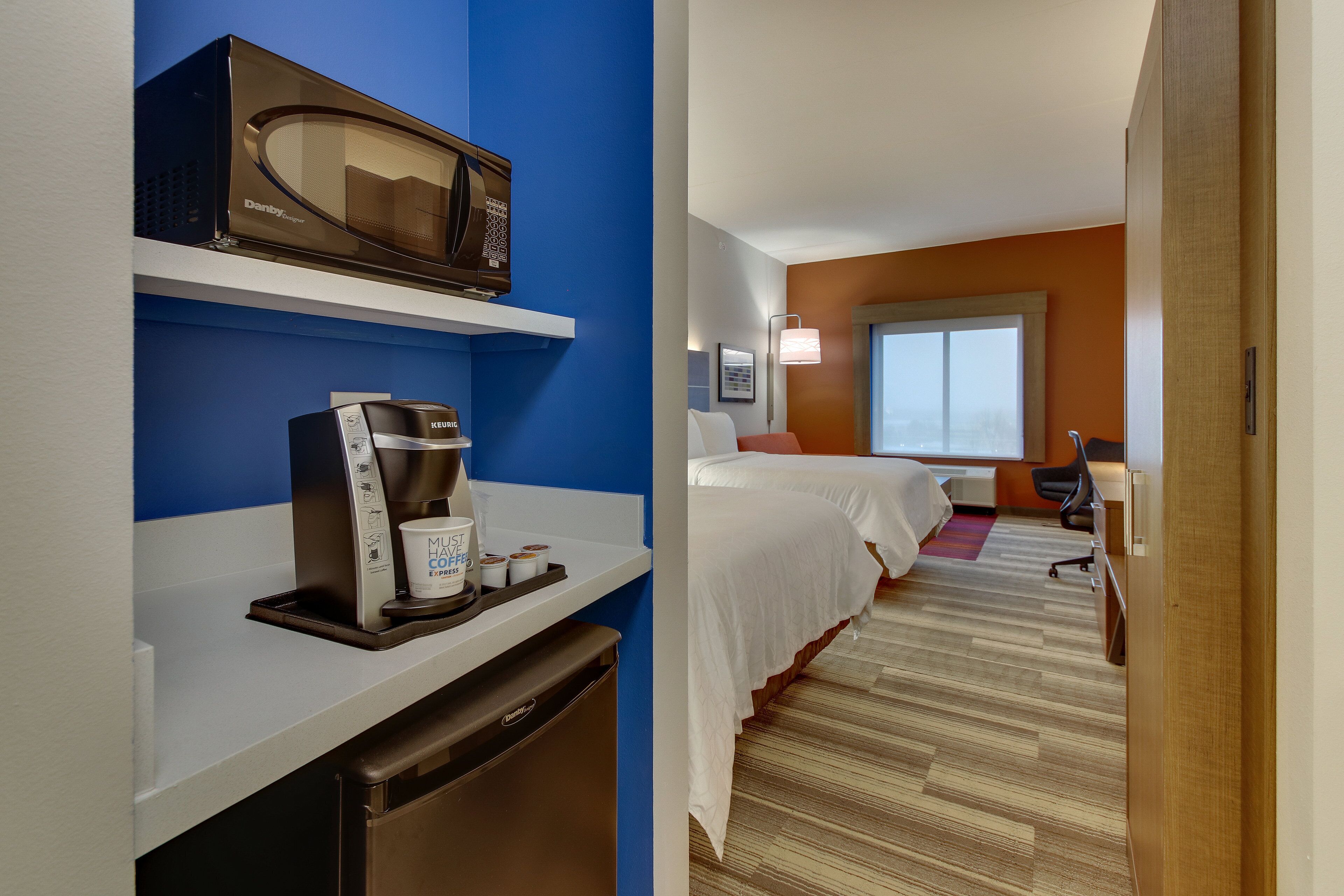 A hotel room with a microwave, coffee maker, and a compact refrigerator. There are two beds with white linens and a window with a view.