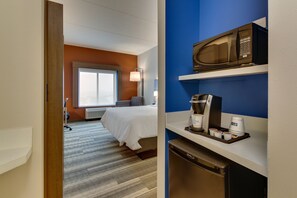 Una habitación de hotel con cama, ventana, microondas, cafetera y lavavajillas.