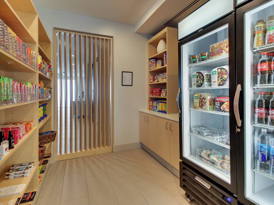 Un pasillo con estantes llenos de refrigerios, un refrigerador para bebidas y una separación con listones verticales.