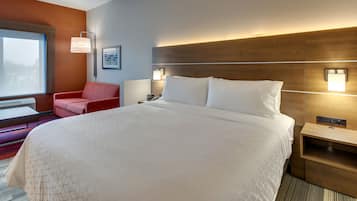 Habitación de hotel con una cama grande, un sillón rojo, una mesita de noche y una lámpara de pared.