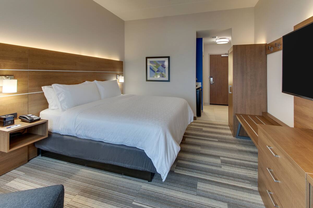 A modern hotel room with a large bed, bedside tables, a flat-screen TV, and a wooden wardrobe.