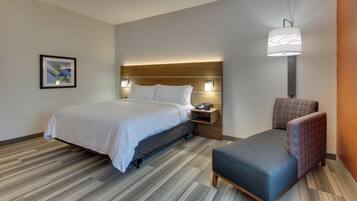A hotel room with a bed, bedside table, lamp, chair, and a framed picture on the wall.