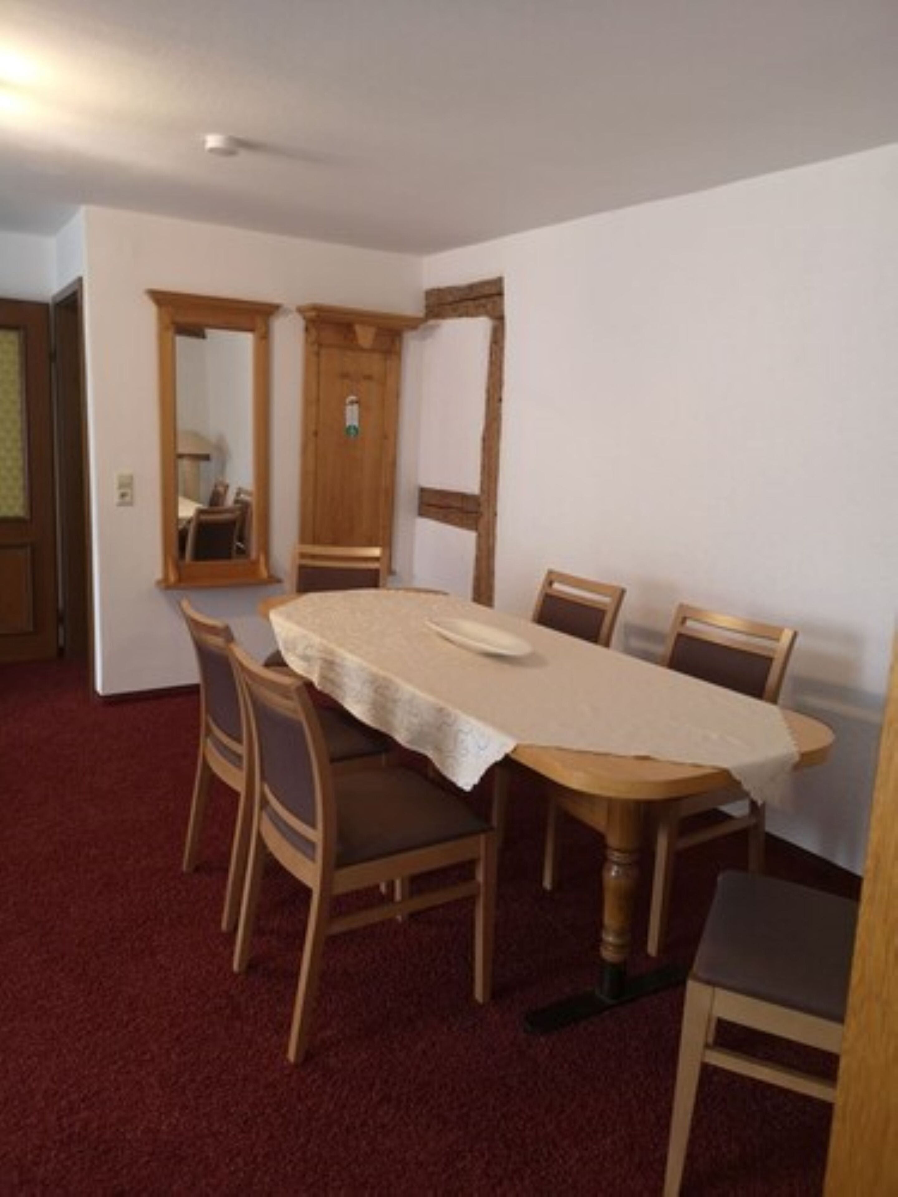 A dining room with a round wooden table, six chairs, and a mirror above the table.