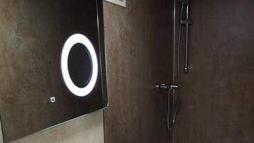 A modern bathroom with a white sink, two rolled towels, a handheld showerhead, and a circular mirror with a light.