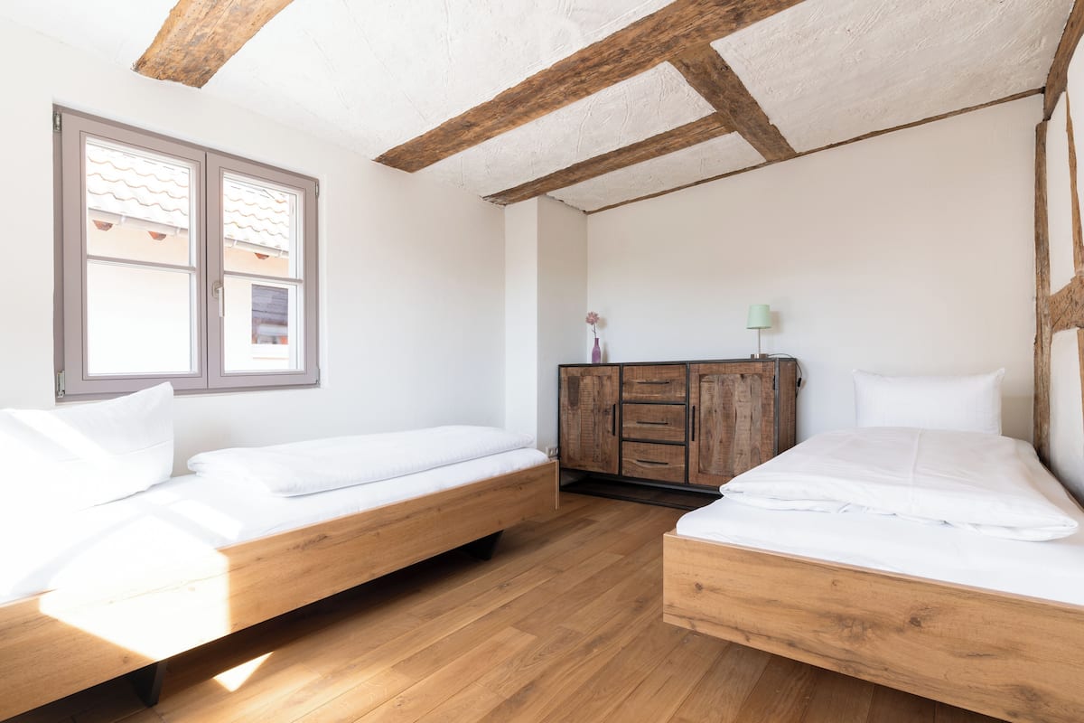 Una habitación con dos camas de madera, un armario de madera y una ventana con contraventanas blancas.