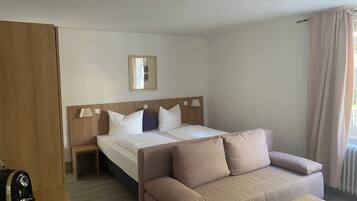A hotel room with a bed, a wooden headboard, a bedside table with a lamp, a sofa, and a coffee maker.