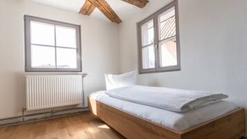 A bedroom with a wooden bed, white bedding, a radiator, and two windows.