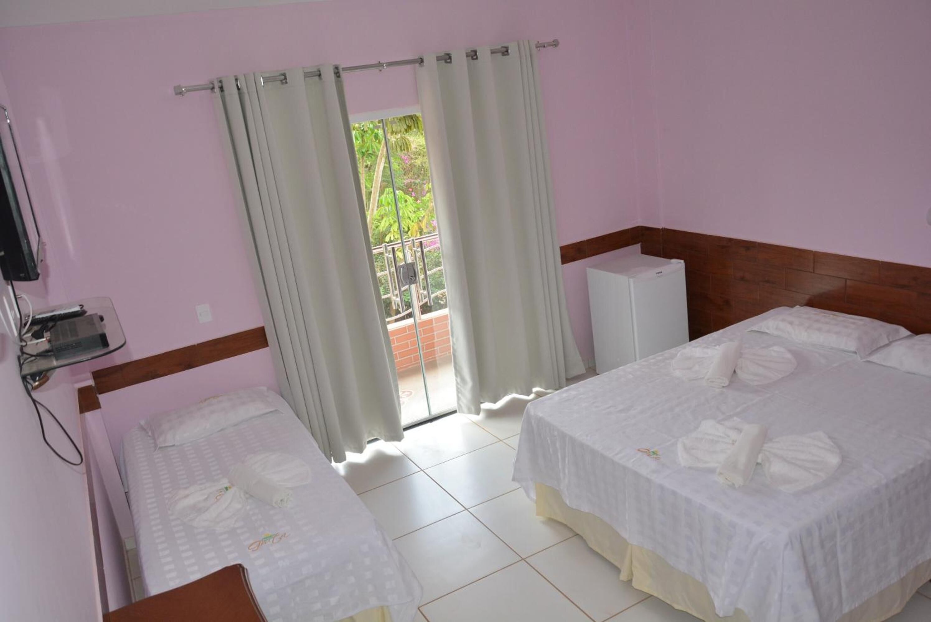 Habitación de hotel con dos camas, un balcón con cortinas, un radiador blanco y un televisor montado en la pared.