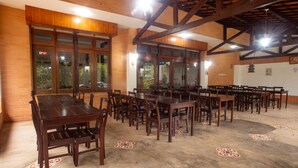 Un vaste espace dédié à la salle à manger, avec de nombreuses tables et chaises en bois, de grandes fenêtres et un sol carrelé orné d’un motif géométrique.