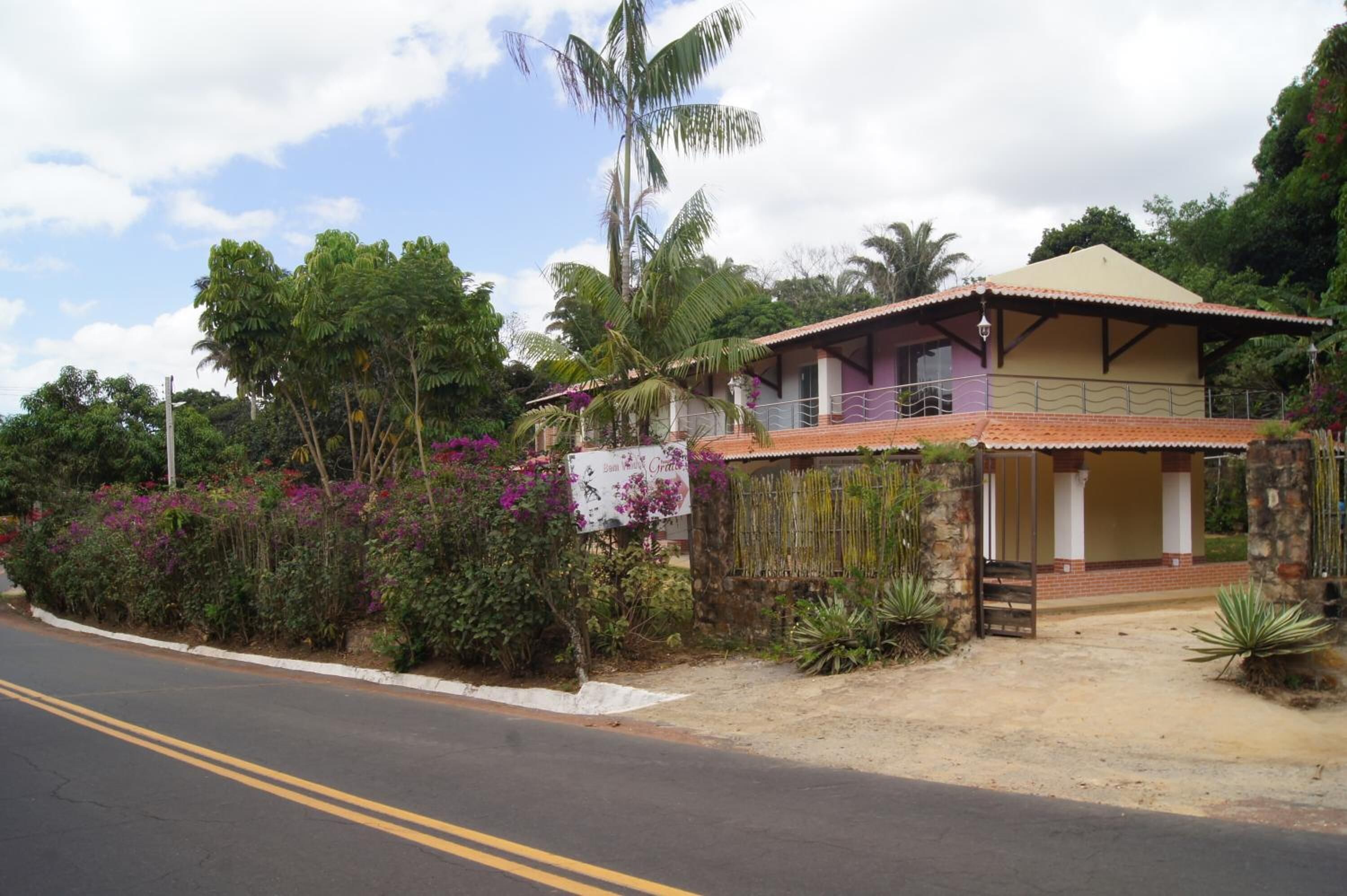 A two-story house with a balcony, surrounded by lush greenery and flowering plants.