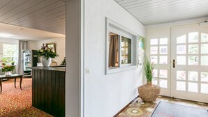 A hallway with a reception desk, a potted plant, and a door with windows.