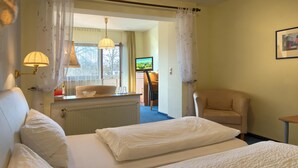 A hotel room with two beds, a sitting area with a chair, a television, and a window with curtains.