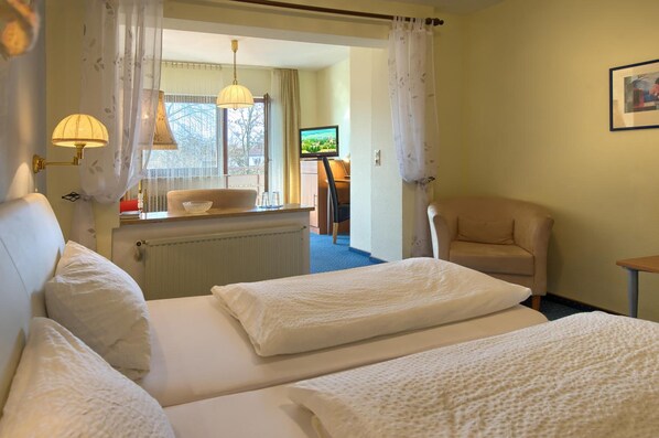A hotel room with two beds, a sitting area with a chair, a television, and a window with curtains.