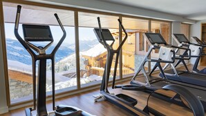 A gym with treadmills and elliptical machines, large windows with a snowy mountain view.
