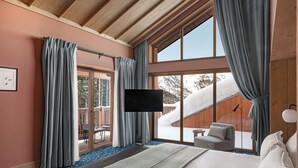 A hotel room with a large bed, a flat-screen TV, a sliding glass door to a balcony, and a view of a snowy landscape.