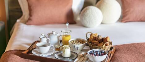 En pænt anrettet bakke med morgenmad på sengen, med puder, en kurv med bagværk, en skål med frugt og en kande appelsinjuice.