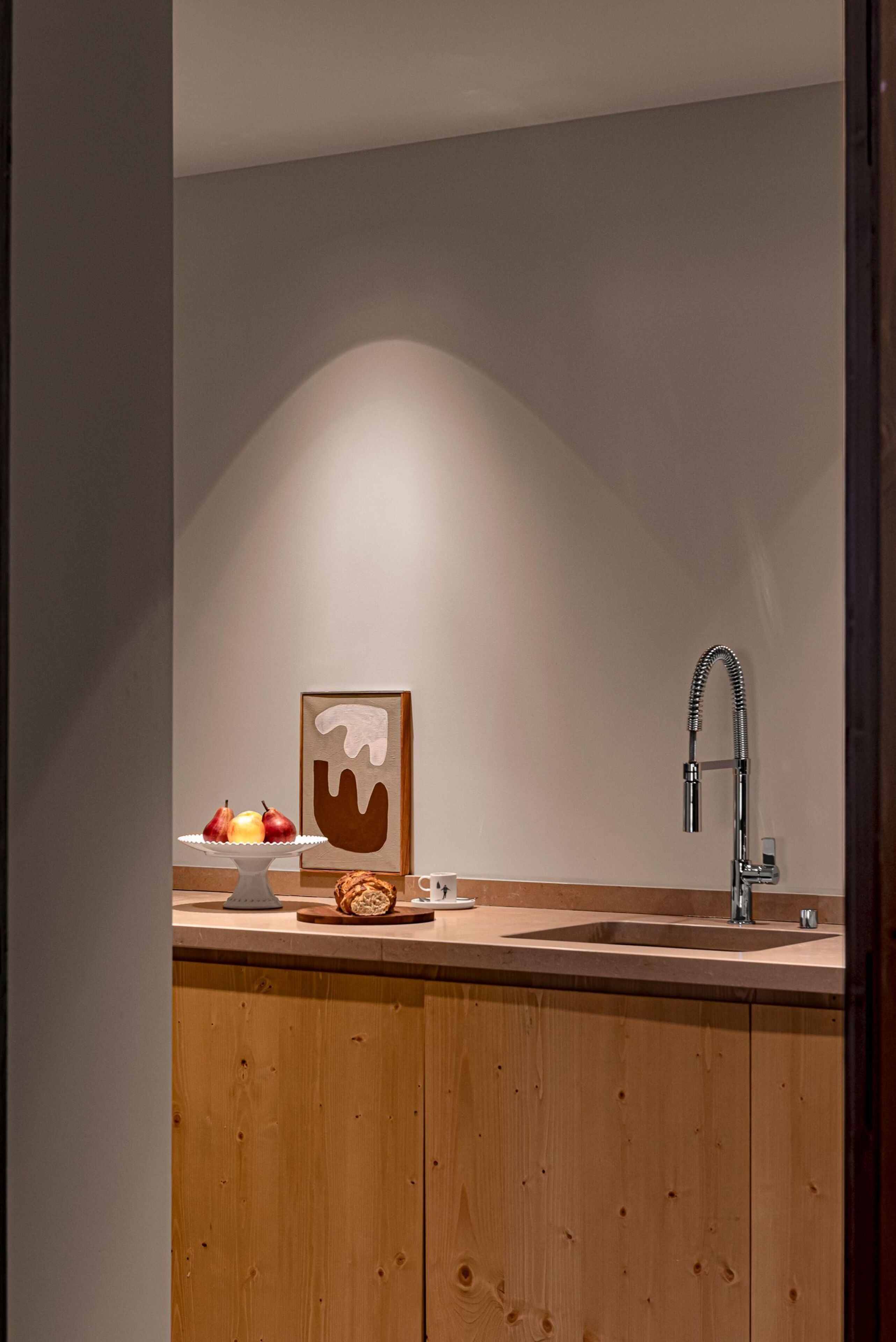 A modern kitchen with a wooden cabinet, a stainless steel sink, and a fruit bowl on the counter.