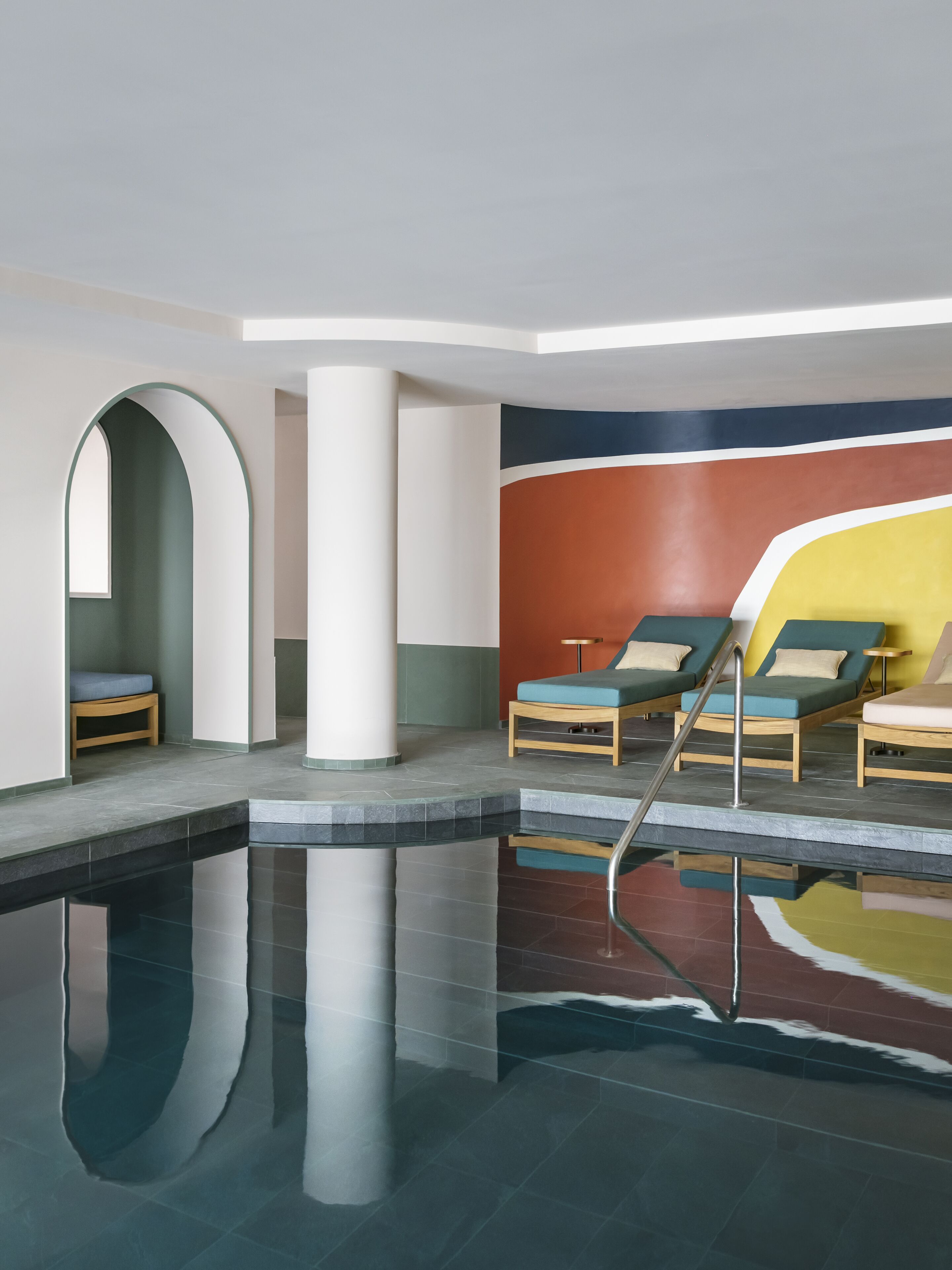 A modern indoor pool area with lounge chairs and a clear pool.