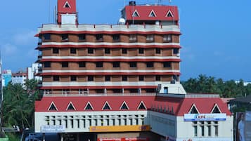 A multi-story hotel with a red and white facade, multiple balconies, and various commercial establishments on the ground floor.