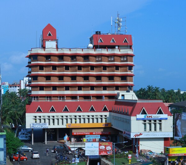 A multi-story hotel with a red and white facade, multiple balconies, and various commercial establishments on the ground floor. - Manuelsons Malabar Palace (Kozhikode)
