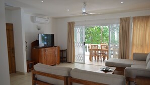 A living room with a television, wooden furniture, and a sliding glass door leading to an outdoor area. - Sundown Beach Villa (Mahé Island)