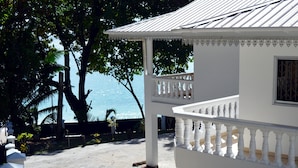 A white building with a balcony, a view of the sea, and a tree in the background. - Sundown Beach Villa (Mahé Island)