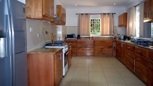 A kitchen with wooden cabinets, a stainless steel refrigerator, a stove, and a window with curtains. - Sundown Beach Villa (Mahé Island)