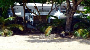 A beachfront property with white buildings, palm trees, and a sandy beach. - Sundown Beach Villa (Mahé Island)