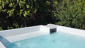 Tinaja rectangular con exterior blanco y calentador integrado, rodeada por una terraza de madera y follaje.