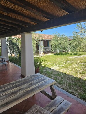 Un patio cubierto con una mesa y sillas de madera, una planta en maceta y vistas a una casa con techo de tejas.