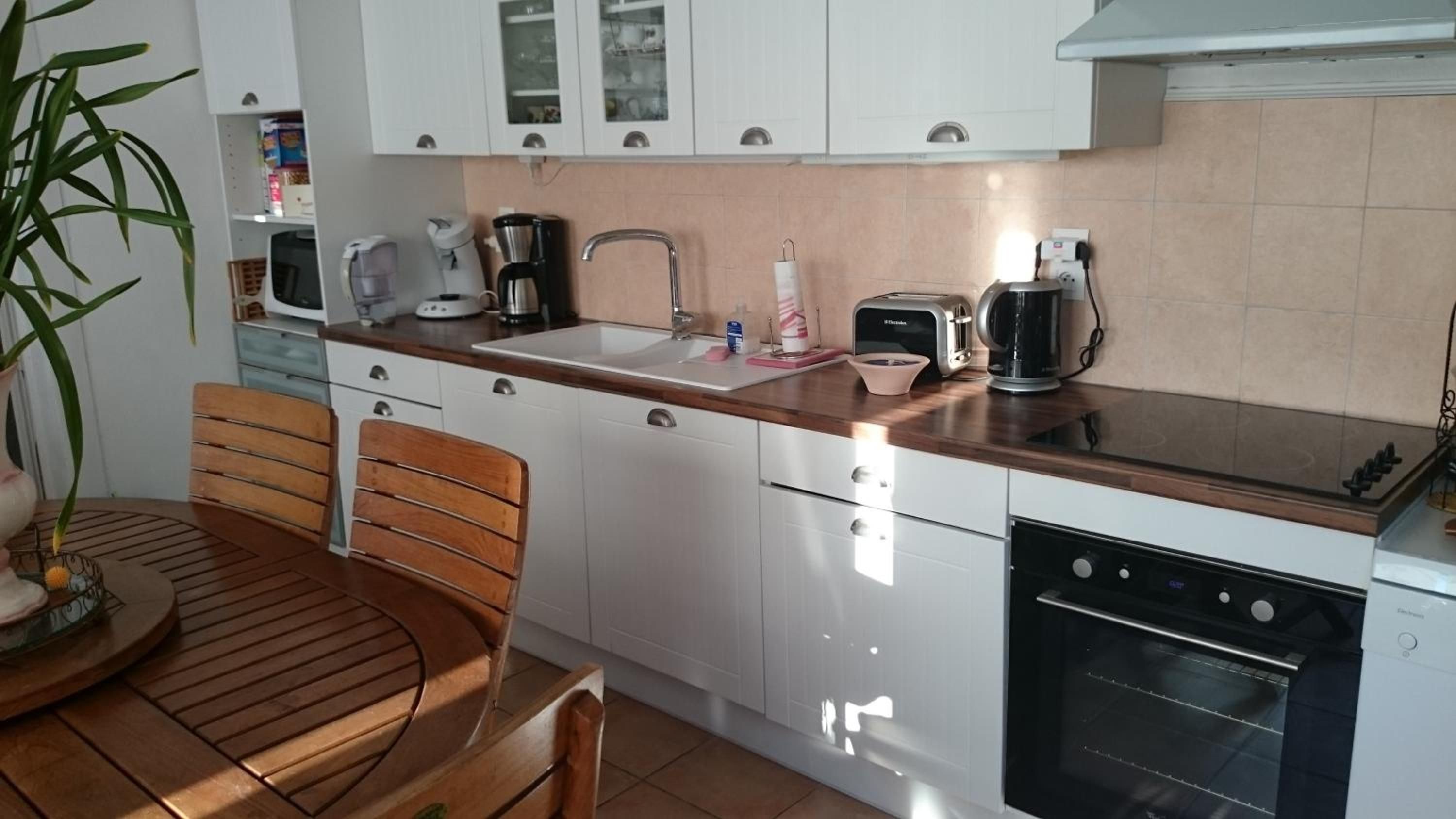 A kitchen with white cabinets, a wooden countertop, a sink, a toaster, a kettle, and a dishwasher.