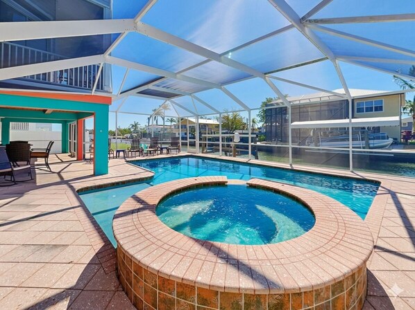 A pool area with a hot tub, lounge chairs, and a covered seating area.