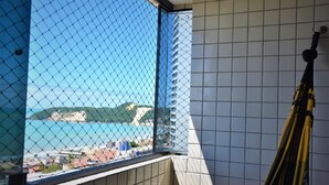 A room with a view of a coastal area through a window with a chain-link fence. - Apartment with a view of Morro do Careca. (NATAL)