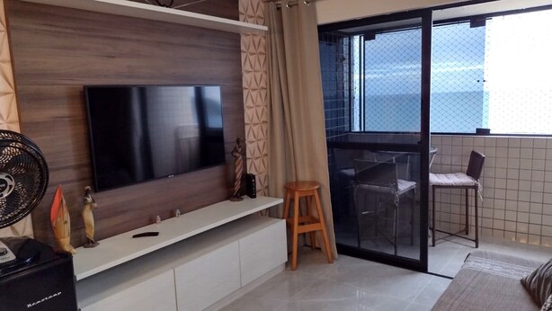 A modern living room with a flat-screen TV, a small table, and a chair. - Apartment with a view of Morro do Careca. (NATAL)