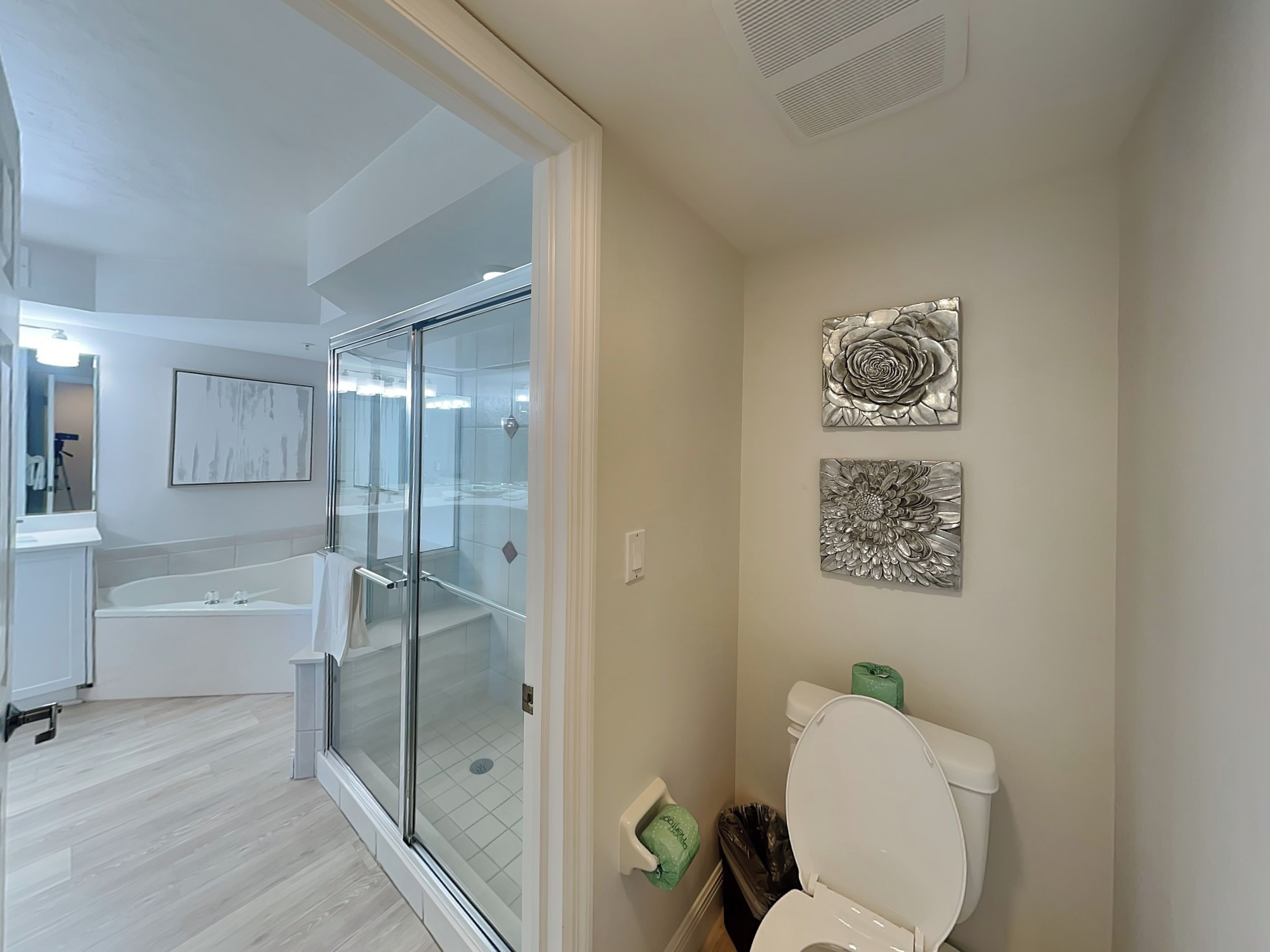 A modern bathroom with a glass-enclosed shower, a white toilet, and two metallic wall art pieces.