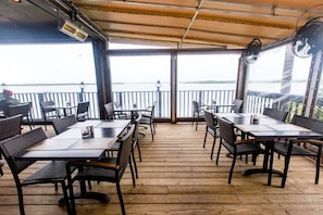 An outdoor dining area with tables and chairs, a wooden deck, and a view of a body of water. - Lovers Key Resort 404 by Distinctive Beach Rentals (Fort Myers Beach)