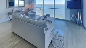 Un salon moderne avec une grande fenêtre, un canapé, un téléviseur et un ventilateur de plafond.