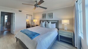 A bedroom with a bed, a nightstand, a ceiling fan, and a window with curtains. - Lovers Key Resort 404 by Distinctive Beach Rentals (Fort Myers Beach)