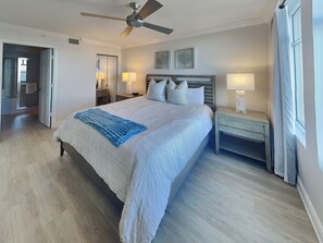 A bedroom with a bed, a nightstand, a ceiling fan, and a window with curtains. - Lovers Key Resort 404 by Distinctive Beach Rentals (Fort Myers Beach)