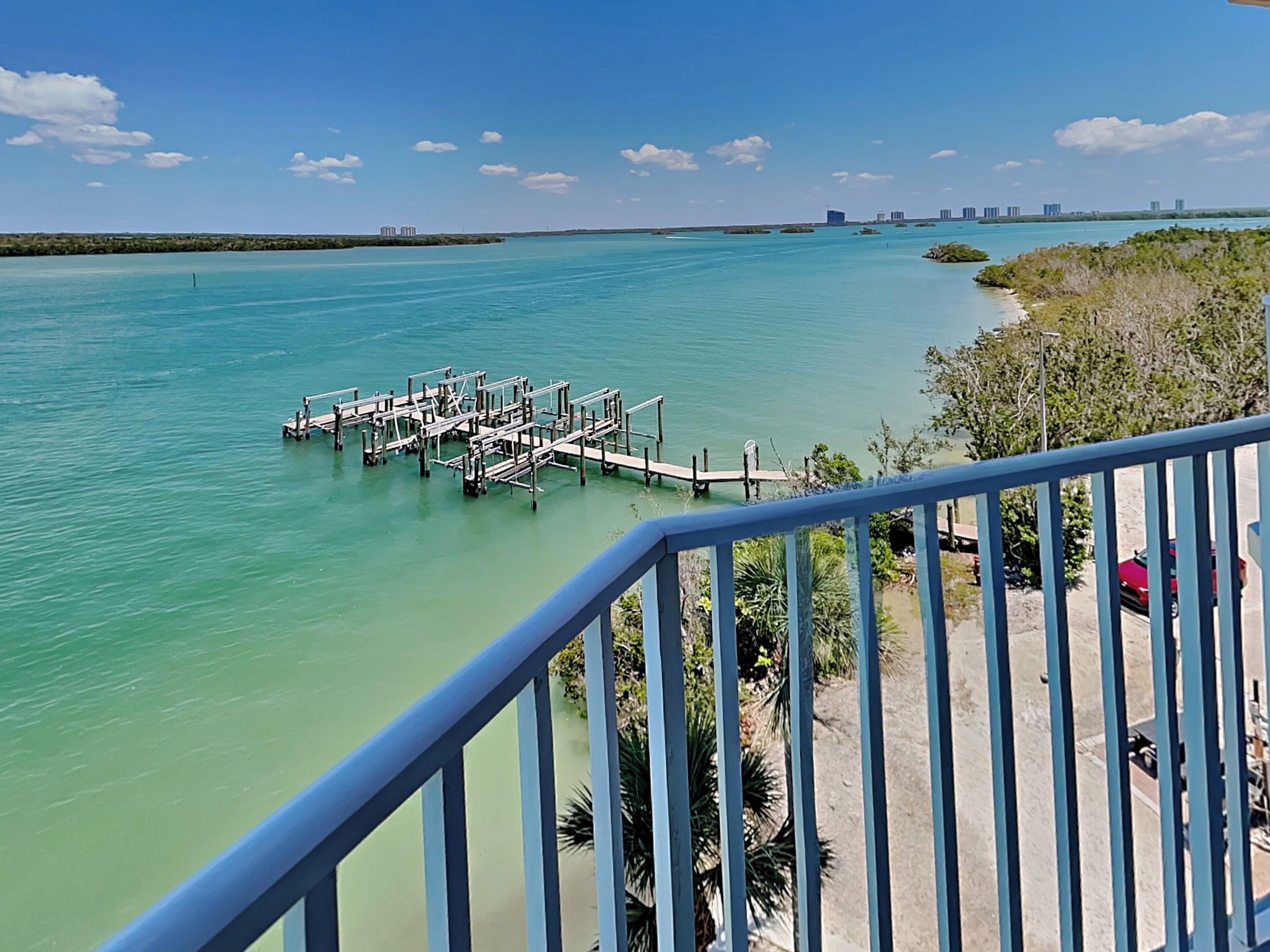 A waterfront view with a dock extending into turquoise water, surrounded by greenery and a clear sky.