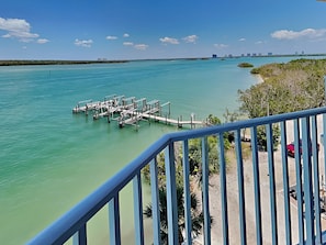 A waterfront view with a dock extending into turquoise water, surrounded by greenery and a clear sky. - Lovers Key Resort 403 by Distinctive Beach Rentals (Fort Myers Beach)
