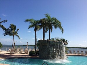 A pool area with a waterfall feature, palm trees, and lounge chairs. - Lovers Key Resort 403 by Distinctive Beach Rentals (Fort Myers Beach)