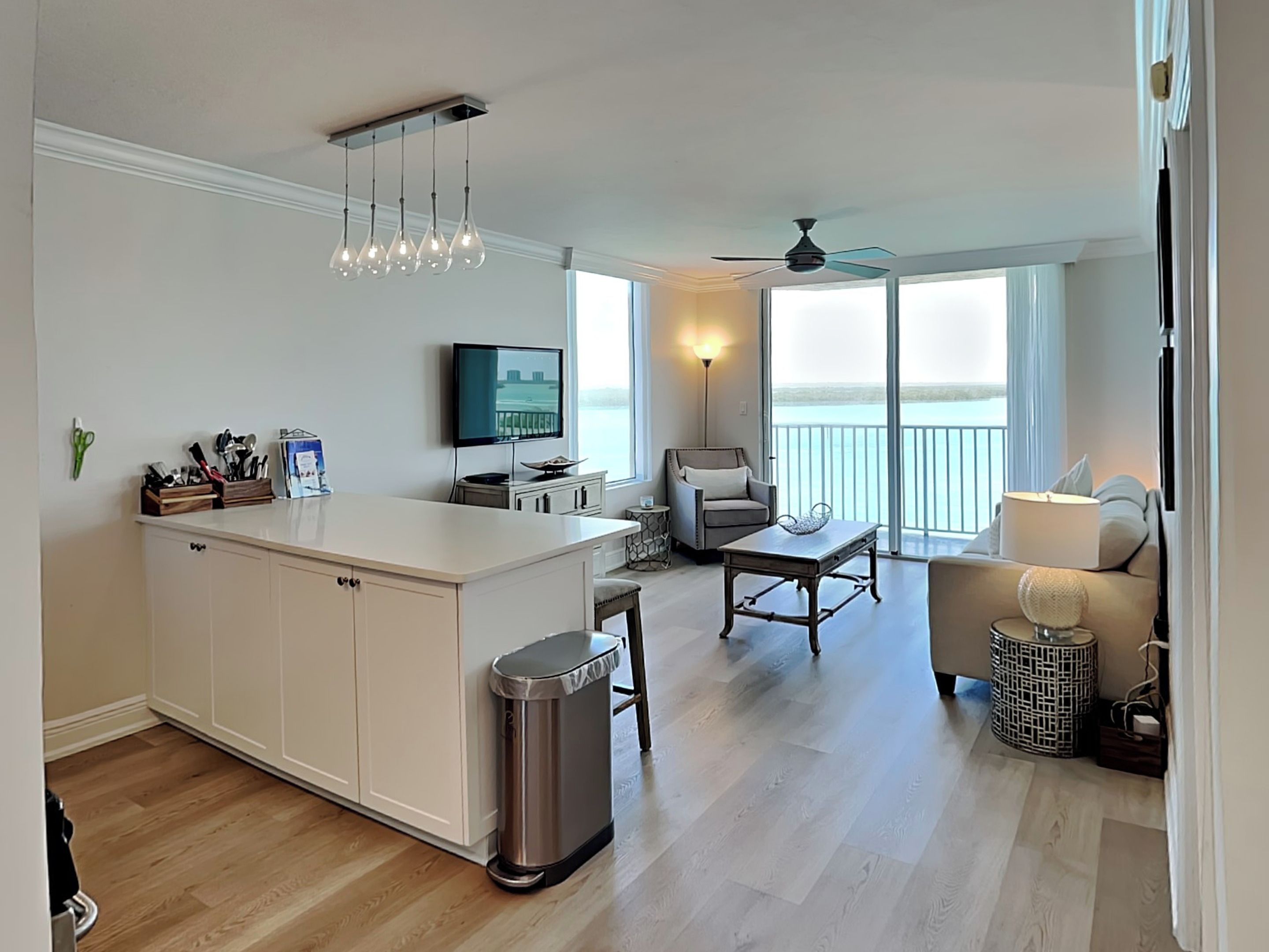 A modern kitchen with a central island, a dining area with a table and chairs, a sofa, and a balcony with a view.