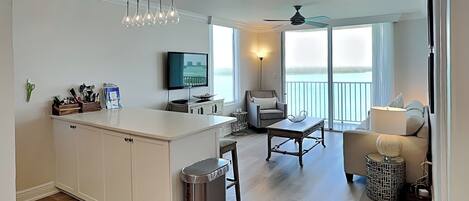 A modern kitchen with a central island, a dining area with a table and chairs, a sofa, and a balcony with a view.