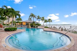 A swimming pool with a 3ft 3in depth, surrounded by palm trees and lounge chairs, with a view of a building and water in the background. - Lovers Key Resort 403 by Distinctive Beach Rentals (Fort Myers Beach)