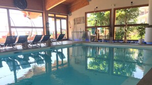 An indoor swimming pool with clear blue water, wooden ceiling beams, and a row of lounge chairs along the side. - Charming cabin studio *** 4/5 pers COZY at 50 m from the slopes (CHAMROUSSE)
